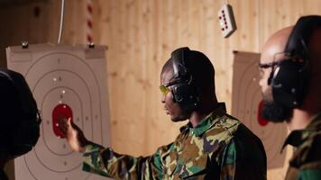 Portrait of happy army soldiers in shooting gallery looking at targets, comparing points obtained. Cheerful military units testing accuracy in firing range, looking at shot bullseye, camera B video