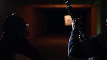 Man holds rifle, enjoying recreational shooting experience in firing range next to group of friends. People practicing with weapons in safe environment at shooting range company, camera B video