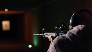 Man in firing range doing shooting activity with rifle, wearing earmuffs to protect hearing. Person training with semiautomatic weapon, using safety gear to prevent damage from gunshots, camera B video