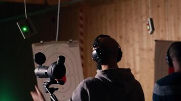 Firing range client doing shooting activity next to friends, zooming to check if he shot bullseye. Person analyzing targets shot using magnifying lens, comparing results with mates, camera B video