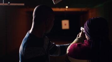 Shooting gallery staff member teaching student how to hold and handle handgun. Firing range expert providing guide to african american woman learning how to achieve proficiency with guns, camera B video