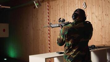 Portrait of happy military personnel using tactical operations equipment, shooting assault rifle. Smiling man in firing range preparing for mission, practicing with semiautomatic weapon, camera A video