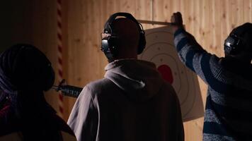 Group of shooting range customers shooting targets with pistols and rifles, learning to operate weapons in close quarters. Friends at shooting ground firing lethal fire handguns together, camera B video