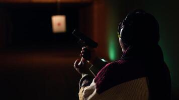 Portrait of joyous shooting range customer shooting targets with pistol, learning to operate handgun in close quarters. Smiling woman at shooting ground facility firing lethal fire weapon, camera B video