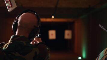 Team of soldiers wearing uniform in firing range doing shooting course to elevate marksmanship skills. Military units in shooting gallery using weapons to engage targets at various ranges, camera B video