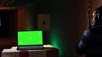Green screen laptop next to shooting gallery safety officer watching client shoot at targets, supervising him. Mockup notebook and firing range expert teaching man how to use firearms, camera B video