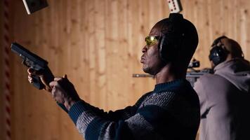 Man holds pistol, enjoying recreational shooting experience in firing range next to instructor reloading weapons. Employee loading firearms for shooting range company customers, camera B video