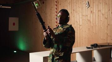 Portrait of cheerful soldier doing training in shooting range, reloading rifle. Joyous military unit in firing range practicing with semiautomatic weapons, wearing protective equipment, camera A video