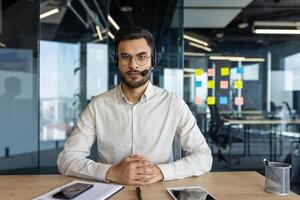 Webcam view, online call. Man with headset calm and confident looking at camera, support worker at workplace. Serious and focused support team member. photo