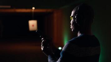 Portrait of happy shooting range customer reloading pistol, shooting targets, having fun. Close up of joyous man at shooting ground facility loading pistol, wearing protection goggles, camera B video