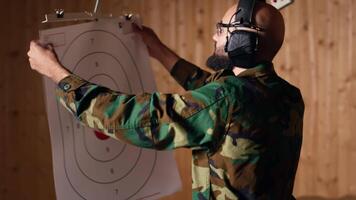Man in firing range shooting targets with pistol, wearing earmuffs to protect hearing. Person training with weapon, hitting bullseyes, using safety gear to prevent damage from gunshots, camera B video