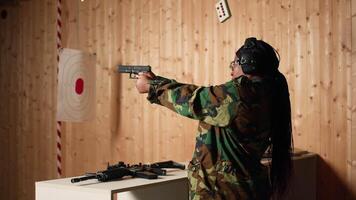Portrait of smiling woman in firing range shooting with pistol, wearing earmuffs to protect hearing. Cheerful person in shooting gallery using safety gear to prevent damage from gunshots, camera A video