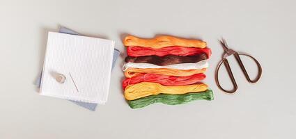 Set of colored floss, canvas and scissors for embroidery on a gray background top view web banner photo