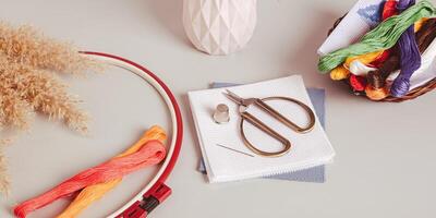 Canvas, embroidery floss, scissors, needle, thimble and cross stitch hoop on table web banner photo