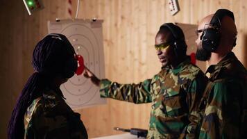 Portrait of joyous army soldiers wearing safety gear in shooting gallery, preparing to fire at targets. Smiling military units in uniform and protection equipment testing accuracy, camera B video