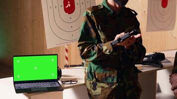 Mockup laptop next to soldiers in shooting range training discussing about weapons. Isolated screen notebook in firing range next to military units having conversation, camera B video