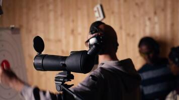 Firing range customer looking in zooming device to check if he shot bullseye next to instructor overseeing client. Person analyzing targets shot using magnifying lens during firearm practice, camera B video