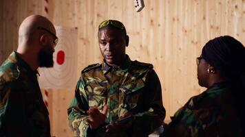 Army commander talking with recruits in shooting gallery, teaching them about weapons handling at close quarters. Military officer instructing soldiers, building combat habits, camera B video