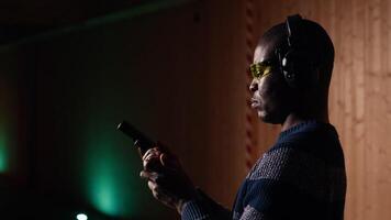 Man in shooting range trying out new gun model before committing to purchase. African american person in indoor firing range learning how to operate new weapon safely, camera A close up video