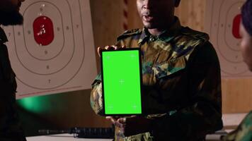 Team of military units at shooting range watching on green screen tablet to learn necessary combat skills. Army soldiers looking at instructions on chroma key device during training, camera B video