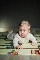A 7-month-old baby is lying on a rug and playing. The child holds his head. A baby learns to crawl on the floor. A child in a beige romper. photo