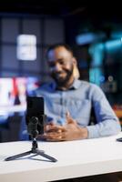 Influencer in blurry background using cellphone to film vlog channel intro for online streaming platforms. Viral media star greets fanbase, presenting today topic, recording with phone photo