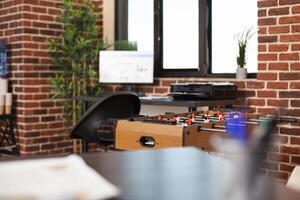 Selective focus on foosball table placed in modern brick wall workspace, ready for employees to unwind. Vacant startup office organized with computer, printer, plants and break area for relaxation. photo