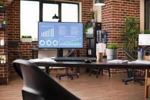 Empty brick wall workspace showing business data analytics on desktop monitor. Well organized shelves, file folders, and plant decor bring a neat, professional look to startup office. photo