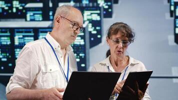 Data storage company executives looking around data center, using laptop and tablet to crosscheck contingency plan and assess high tech workspace units in need of fixing, preventing liabilities photo