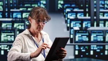 Hardworking supervisor in server room housing high end machines capable of quickly and efficiently performing complex computations and data analysis, using tablet to stop failures photo