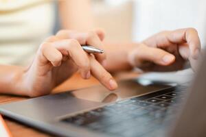 Hands typing on a laptop keyboard with a pen, representing digital work and communication. photo
