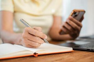 Person multitasking with smartphone and notebook at a desk, symbolizing productivity and modern work habits. photo