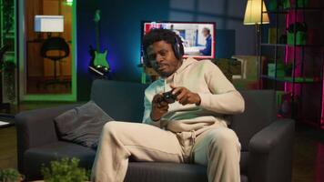 African american man plays intense online games at home, spamming attack buttons on his controller. Gamer participating in online competition, playing on gaming console. Camera B. video
