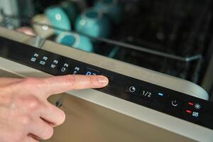 Finger pressing button on dishwasher control panel photo