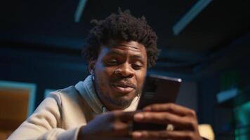 African american young adult enjoying a break from remote work and texting, having fun on social media apps with his friends. Freelancer relaxing and scrolling websites on phone. Camera B. video