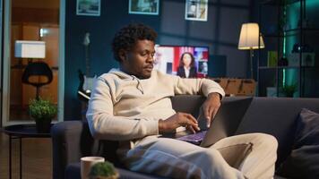 Black man does his research by reading articles and taking notes at home, collecting information for a new project. Freelancer multitasking and studying files with data driven papers. Camera B. video