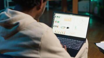 avlägsen arbetstagare revisor håller på med matematik beräkningar använder sig av finansiell grafer på bärbar dator, arbetssätt på Hem. själv sysselsatt kille i loft jämförande företag ekonomisk siffror på anteckningsbok. kamera a. video