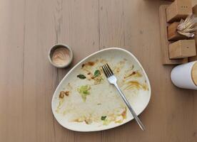 Dirty plate after dinner. Top view of dirty white plate with fork over wooden tabletop. Dirty plate after eating salad with sauce on the dining table. Copy space photo