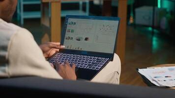 African american freelancer working from home using financial graphs, reviewing statistical data to compare supply and demand numbers. using business charts and writing on notepad. Camera A. video