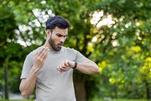 Close-up photo of a shocked and disappointed young Indian man looking at the smart watch on his wrist after jogging and exercising.