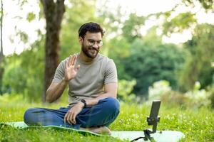 Man actively participating in online fitness session in serene park setting using phone. Shows enthusiasm and engagement with fitness routine in natural surroundings photo