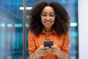 Close-up portrait of a woman with a mobile phone in her hands. Businesswoman smiling and looking at the camera using an application on a smartphone, successful office worker at the workplace. photo