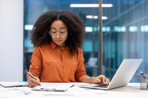 Serious accountant doing paperwork, woman working with documents, contracts and invoices. Office worker at work with laptop filling out financial reports. photo