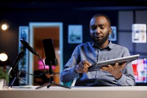 Influencer in home studio using smartphone on phone holder to record live broadcast, reviewing laptop. Online show host filming electronics haul, presenting notebook for viewers using cellphone camera photo