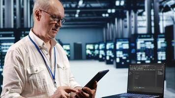 IT solutions expert in data center environment, solving tasks on tablet while running scripts on laptop terminal. Skilled specialist amidst servers, accessing databases and manipulating lines of code photo