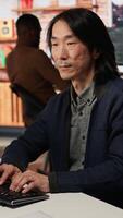 Vertical Portrait of smiling senior engineer coding advanced AI algorithm in startup office, refining machine learning models. Cheerful man using coding platform in Silicon Valley workplace, camera A video