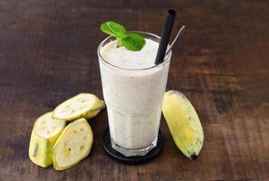 Banana milkshake with sliced fresh bananas isolated on wooden table photo