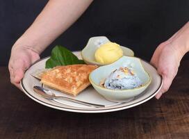 Hands hold dish with organic ice cream and Belgium waffles on wooden table background photo