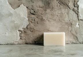 A bar of soap sits on a rustic surface against a textured wall photo