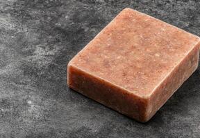 A square bar of exfoliating soap sits on a dark gray surface photo